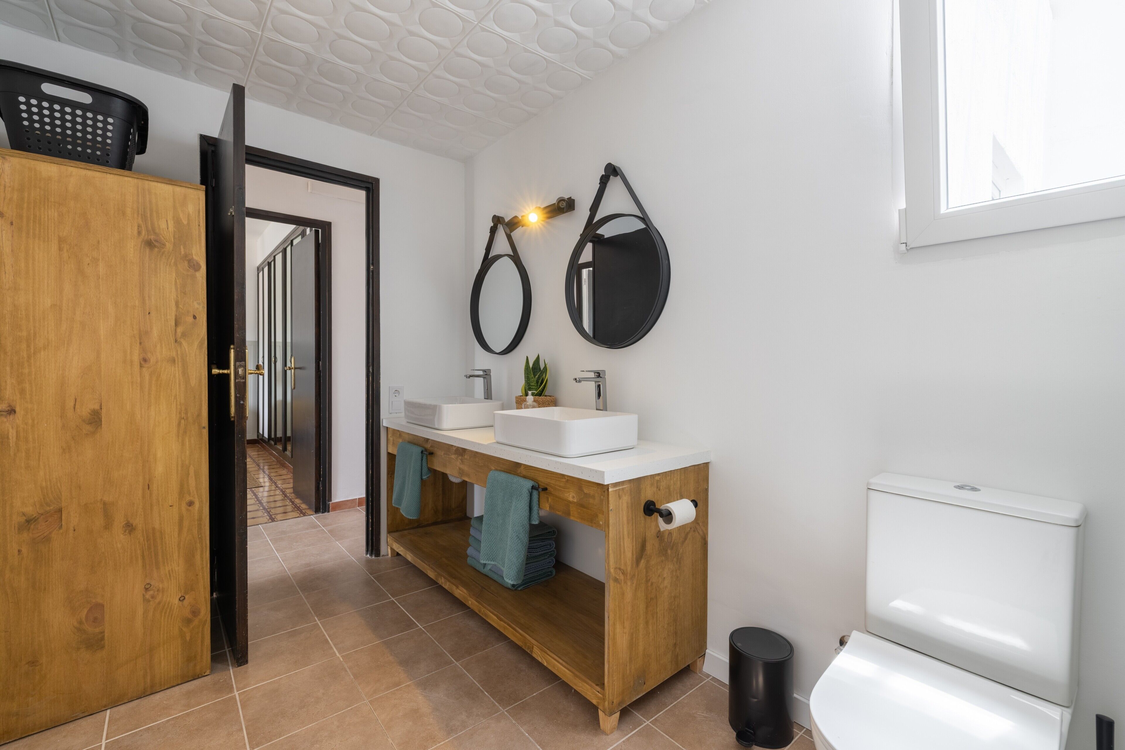 A bathroom with a wooden vanity, two sinks, a toilet, and a mirror.
