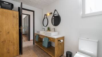 A bathroom with a wooden vanity, two sinks, a toilet, and a mirror.