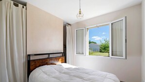 A bedroom with a bed, curtains, a window, and a hanging light fixture.