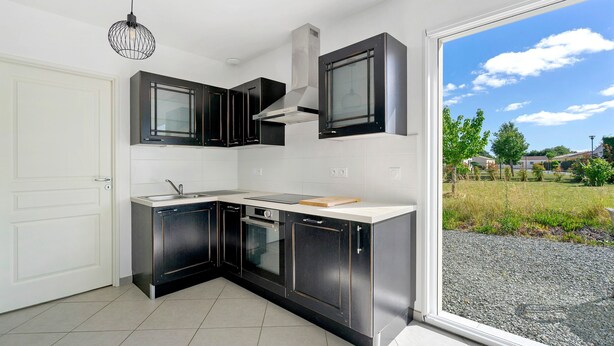 A modern kitchen with black cabinets, a stainless steel range hood, and a large window offering a view of a grassy area.