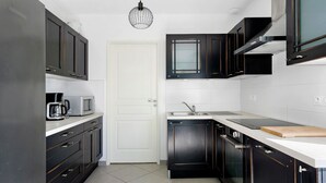 A modern kitchen with dark cabinetry, a white door, a microwave, a coffee maker, a sink, and a cutting board.