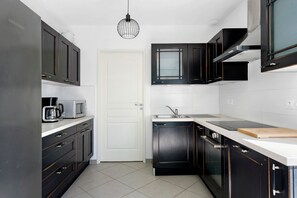 Une cuisine moderne avec des meubles de couleur sombre, une porte blanche, un four à micro-ondes, une machine à café, un évier et une planche à découper.