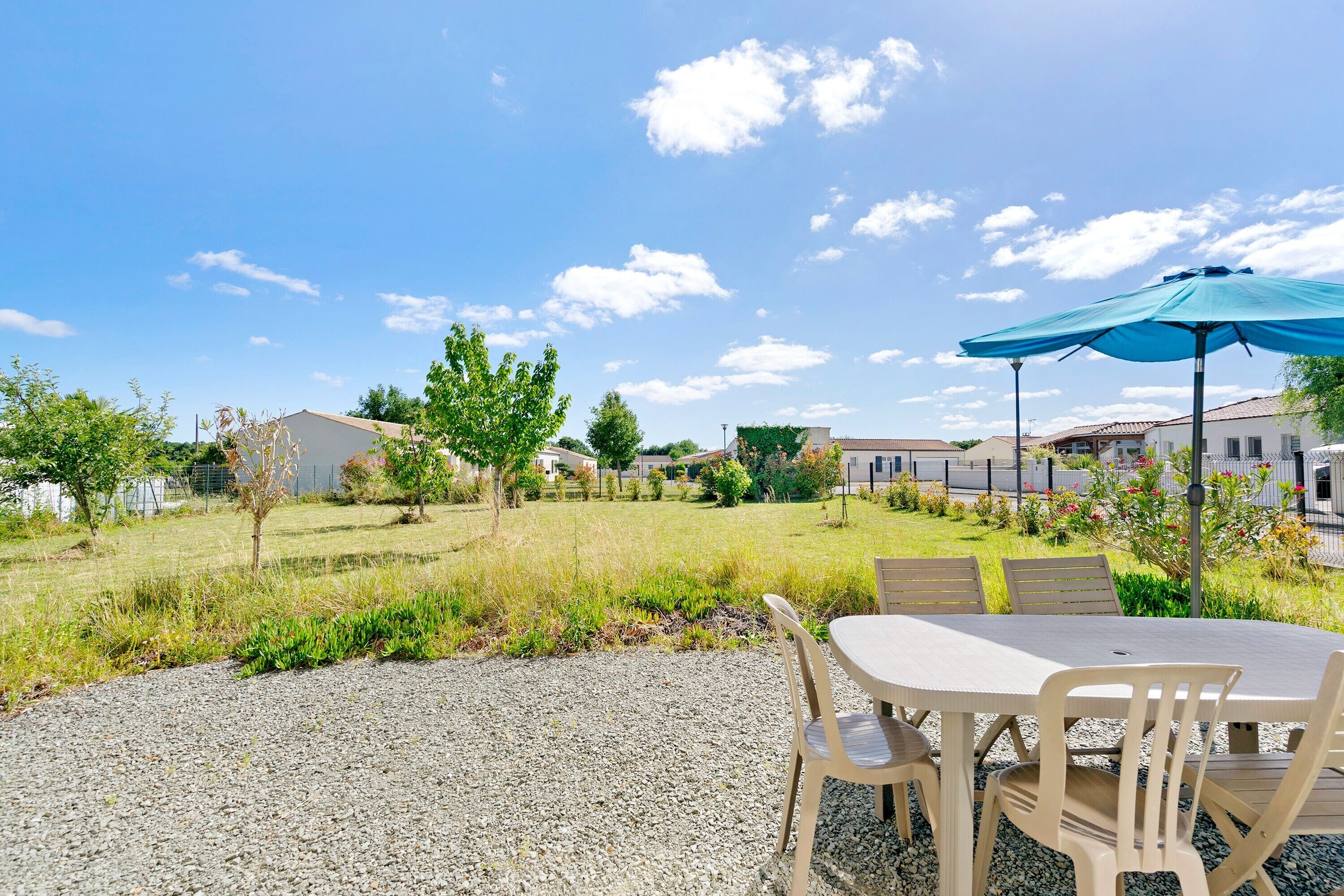 A patio area with a table and chairs, a blue umbrella, and a view of houses in the background.