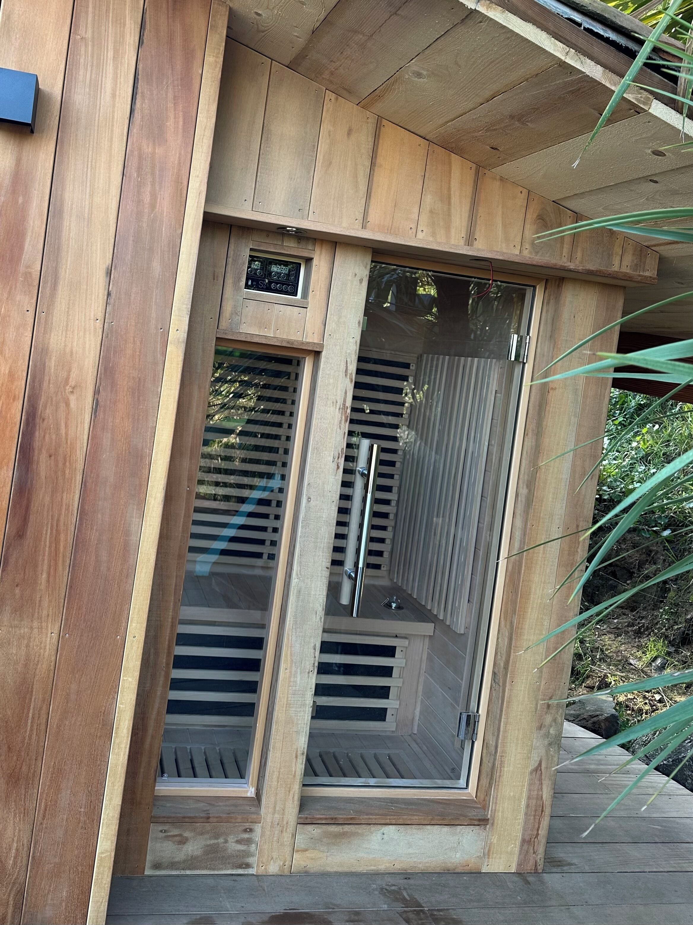 Eine Holzhütte mit Glastür und Metallgriffen, vermutlich eine Sauna oder ein Dampfbad.