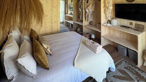 Ein Schlafzimmer einer Holzhütte mit einem Bett, Kissen, einer Pendelleuchte, einem Fernseher und Holzregalen.