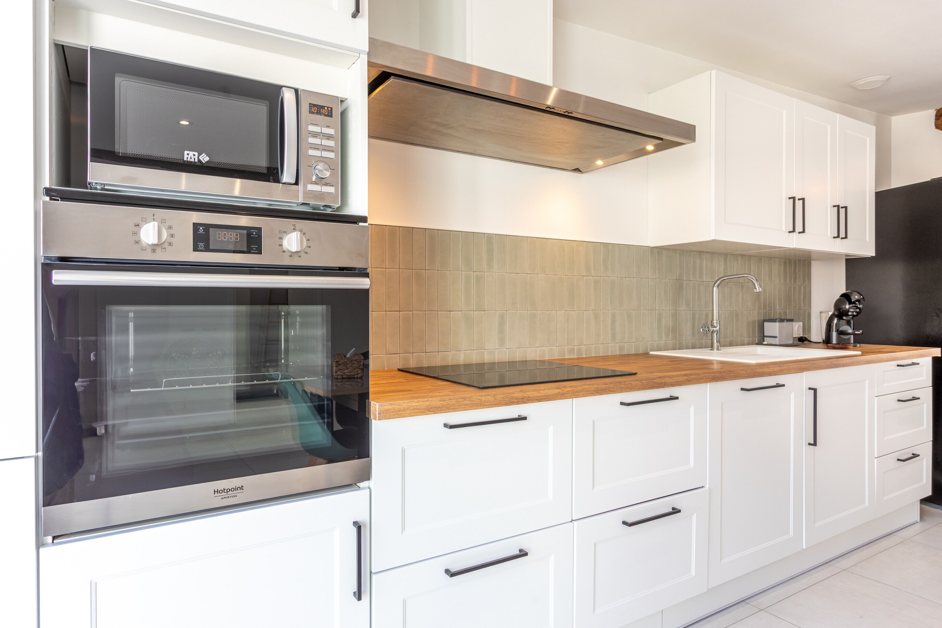 A modern kitchen with stainless steel appliances, white cabinetry, and a wooden countertop.