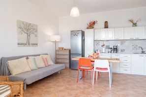 A modern kitchen with white cabinets, a grey sofa, orange chairs, and a dining table.