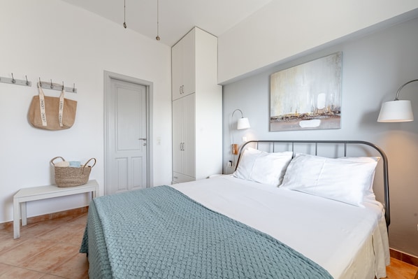 A bedroom with a bed, a bench, a wall-mounted lamp, a painting, and a door.