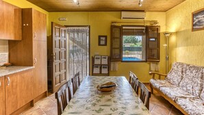 A dining area with a table, chairs, a sofa, wooden cabinets, a window, and an air conditioning unit. - Apartment 'Cal Ferrer 2 - Quadres' with Shared Pool, Wi-Fi and Air Conditioning (Unknown)