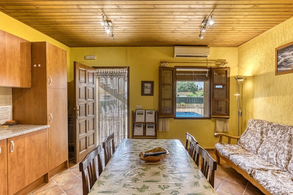 Un espace repas comprenant une table, des chaises, un canapé, des meubles en bois, une fenêtre et un appareil de climatisation.