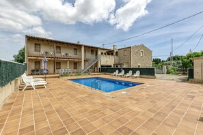 Une piscine avec un revêtement de sol en carrelage, un espace extérieur aménagé pour s’asseoir et un bâtiment doté d’une façade en pierre.