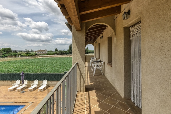 Una terraza con piscina, sillas de descanso y vista a un campo.