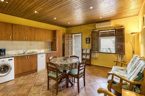 Una cocina con armarios de madera, lavadora, mesa de comedor con sillas y un sofá.