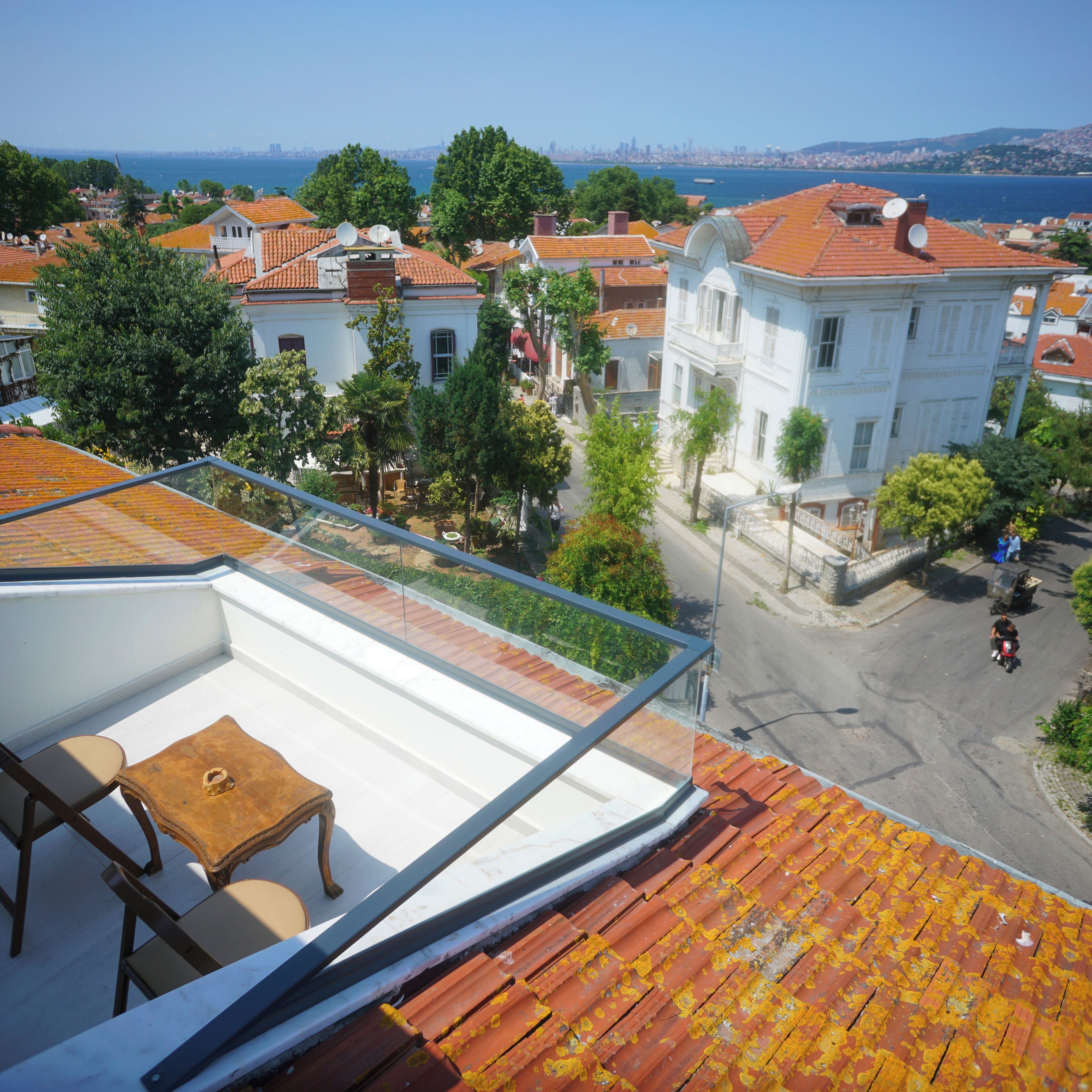 A rooftop terrace with a table and chairs, overlooking a coastal cityscape with traditional buildings and a view of the sea.