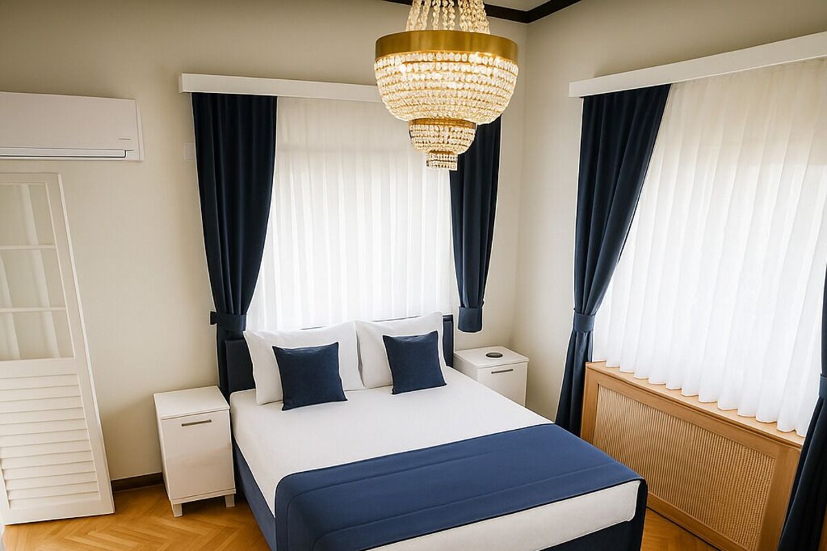 A bedroom with a bed, nightstands, a chandelier, and a window with curtains.
