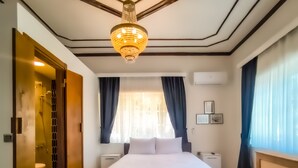 A modern hotel room with a large bed, a walk-in closet, a bathroom, and a chandelier. - Palm Villa  (Adalar)