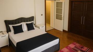 A bedroom with a bed, nightstands, a chandelier, a wardrobe, and a door leading to another room.