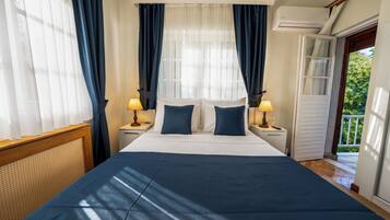 Habitación de hotel con cama, dos mesitas de noche, ventana con cortinas, equipo de aire acondicionado y puerta que da a un espacio exterior.