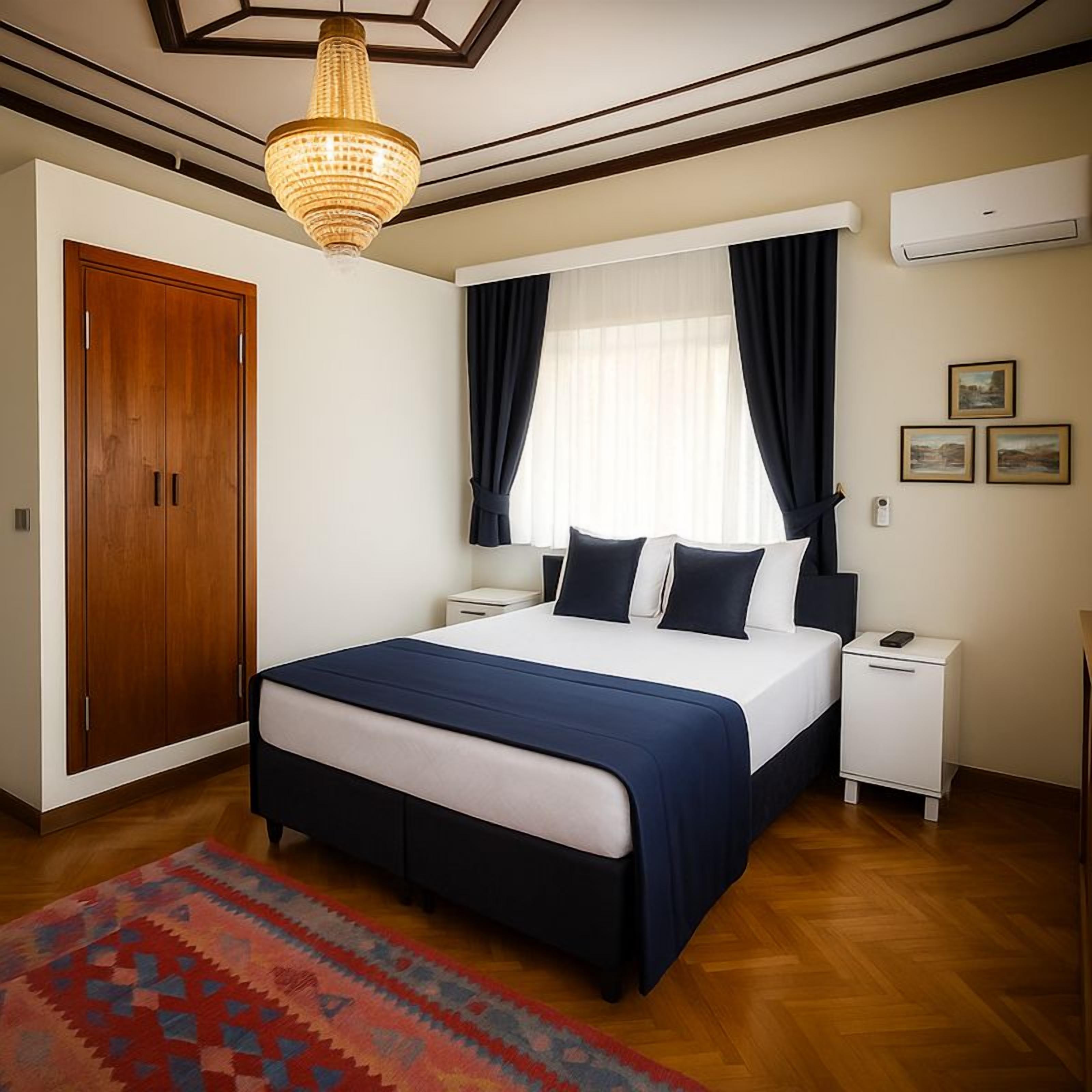 Ein Hotelzimmer mit Bett, Nachttischen, einem Holzschrank, einer Deckenleuchte und einem Fenster mit Vorhängen.