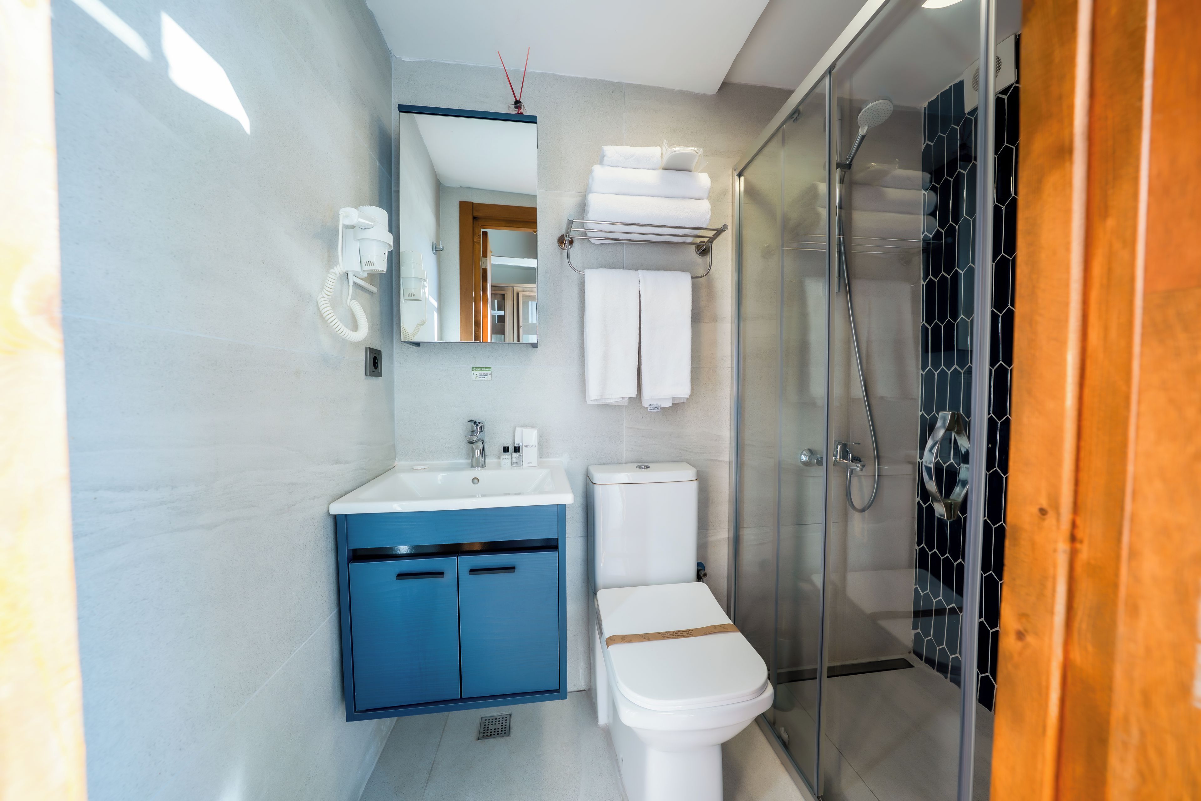 Une salle de bain moderne avec une douche à parois de verre, des toilettes blanches, un meuble-lavabo bleu et un téléphone fixé au mur.