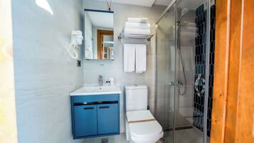 Une salle de bain moderne avec une douche à parois de verre, des toilettes blanches, un meuble-lavabo bleu et un téléphone fixé au mur.