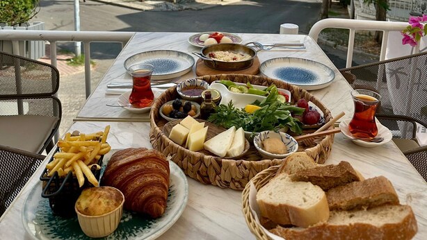 A table with food, a view of a street, and a building in the background. - Palm Villa  (Adalar)