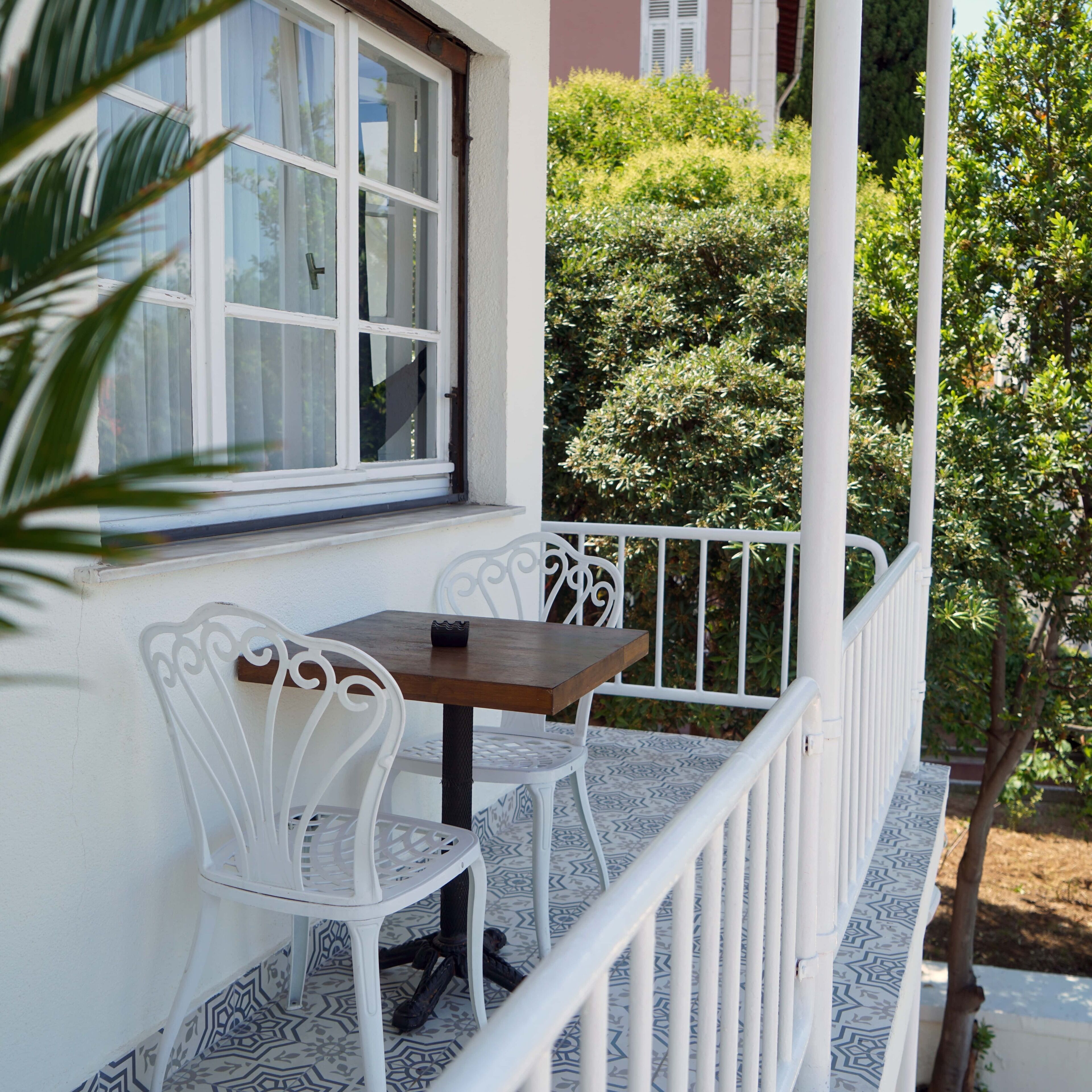 Ein Balkon mit weißer Brüstung, einem kleinen Tisch und zwei weißen Stühlen.