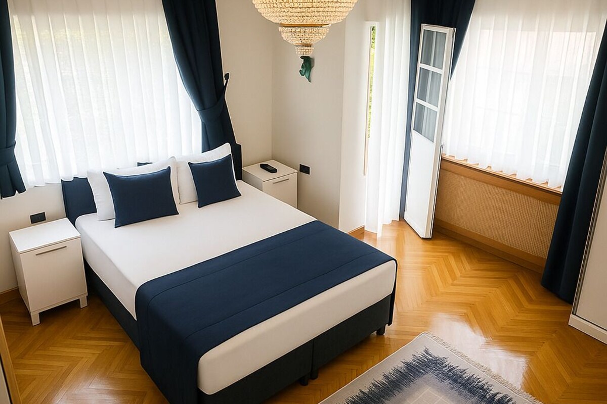 A bedroom with a large bed, bedside tables, a chandelier, and a view through the window.