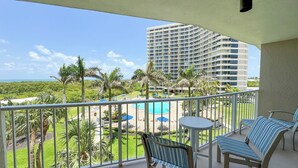 A balcony with a pool, lounge chairs, and a view of a high-rise building and beach. - South Seas Tower 3-401: Marco Island Rental Properties (Marco Island)