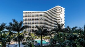 A multi-story hotel with a curved facade, a pool area with lounge chairs, and palm trees in the foreground. - South Seas Tower 3-401: Marco Island Rental Properties (Marco Island)