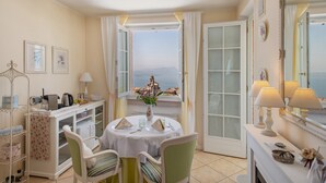 A dining area with a table set for two, a view of the sea, and a white cabinet with kitchen items. - Room 'Gemme Suite Bb' with Lake View, Balcony and Wi-Fi (Torri del Benaco)