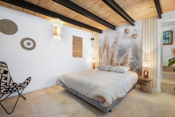 A bedroom with a bed, a chair, wall decor, and a window.