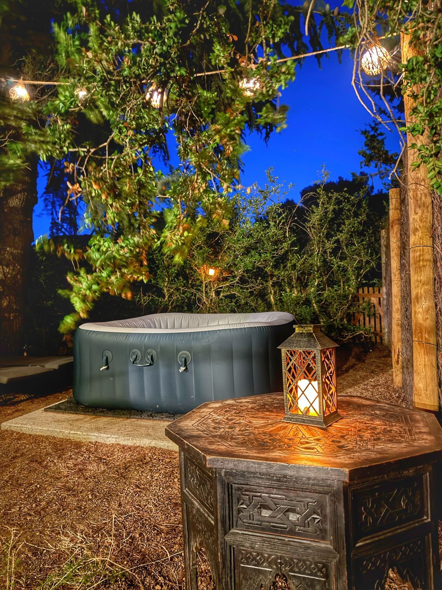 A hot tub and a lantern on a wooden table in an outdoor setting at night.
