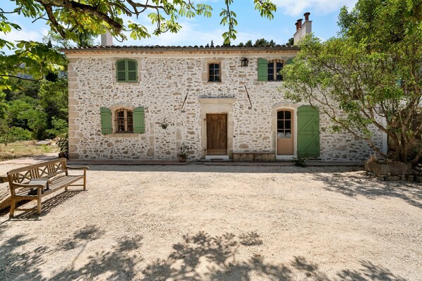 A stone building with a gravel driveway, a wooden bench, and a door.