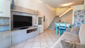 A living room with a TV, sofa, and staircase. - Holiday Home 'Elisa' with Wi-Fi and Air Conditioning (Viddalba)