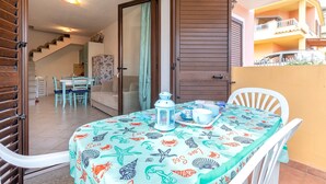 A dining area with a table set for two, a white chair, a white tablecloth with sea-themed designs, a lantern, and a door leading to a staircase. - Holiday Home 'Elisa' with Wi-Fi and Air Conditioning (Viddalba)