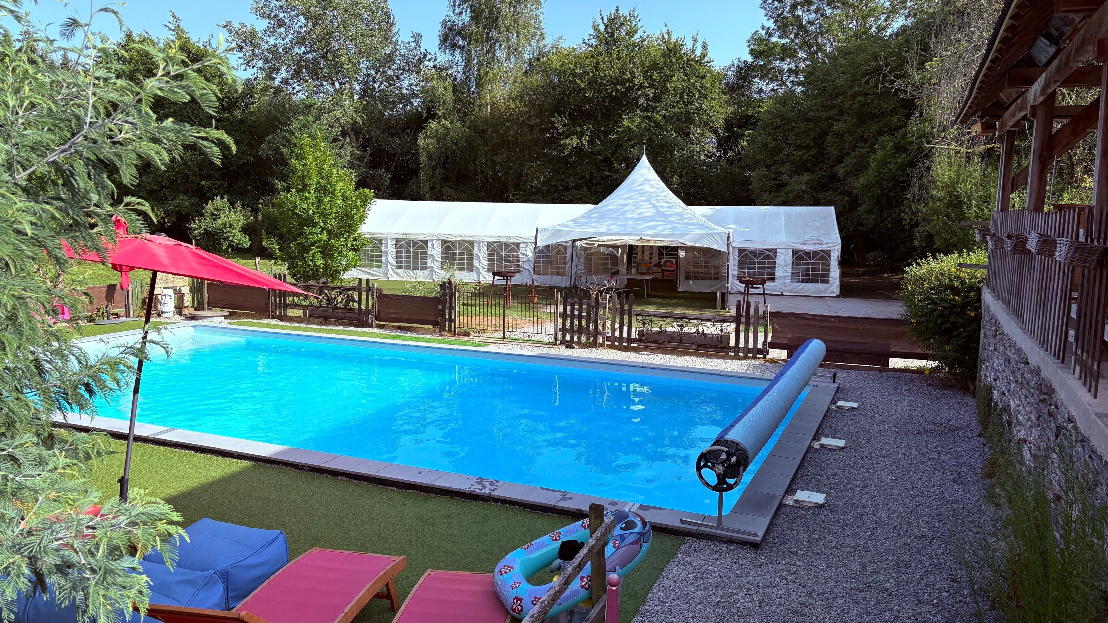 Ein Swimmingpool mit rotem Sonnenschirm, Liegestühlen und einem Zelt im Hintergrund.