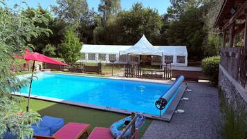 Ein Swimmingpool mit rotem Sonnenschirm, Liegestühlen und einem Zelt im Hintergrund.