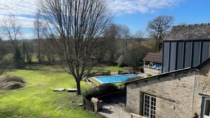 A stone building with a swimming pool, surrounded by a grassy yard and trees.