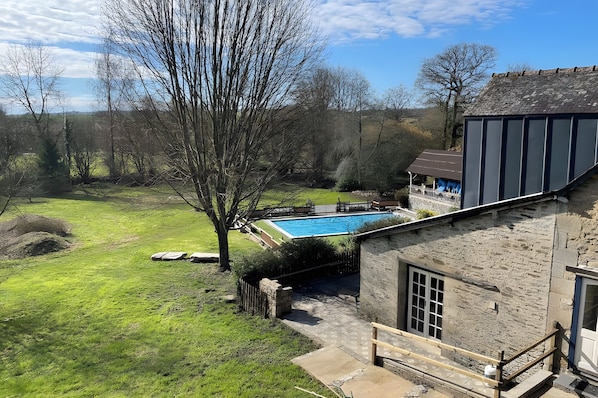 Un bâtiment en pierre doté d’une piscine, entouré d’une cour verdoyante et d’arbres.