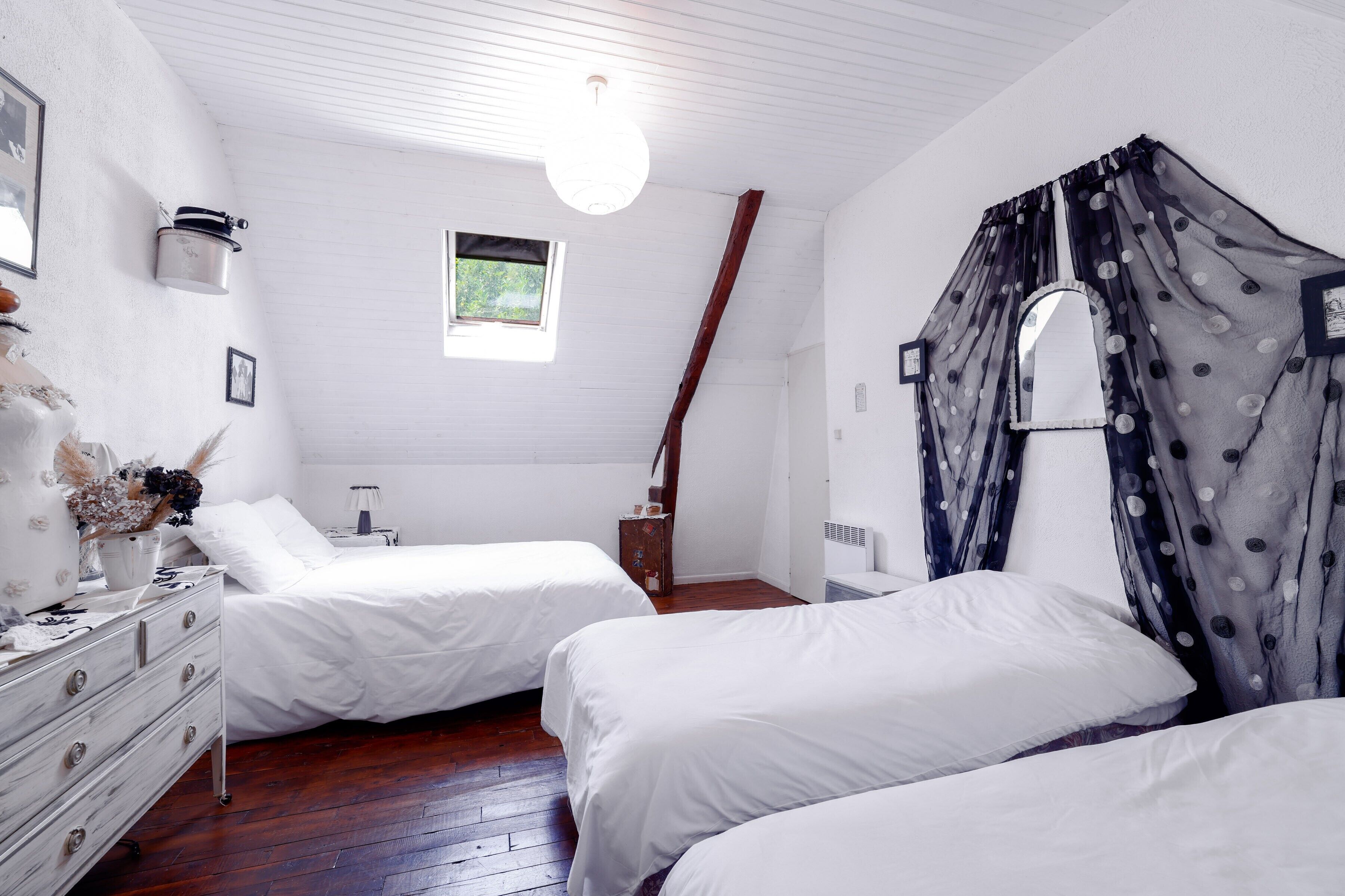 Een slaapkamer met twee bedden, een dressoir, een raam en een plafondlamp.