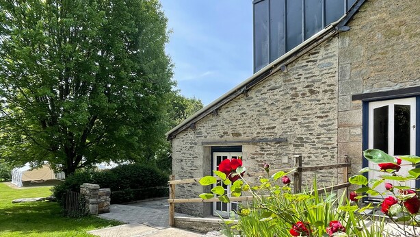 Un edificio de piedra con una puerta de madera, un muro de piedra y un césped con flores rojas.