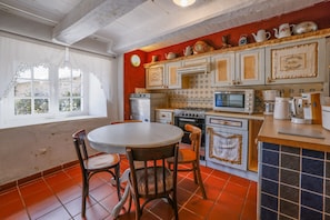 Una cocina con una mesa redonda, sillas y un ventanal con cortinas.