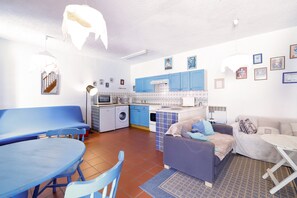 Um espaço habitacional compacto com área de jantar, sofá, cozinha pequena com armários azuis e máquina de lavar.