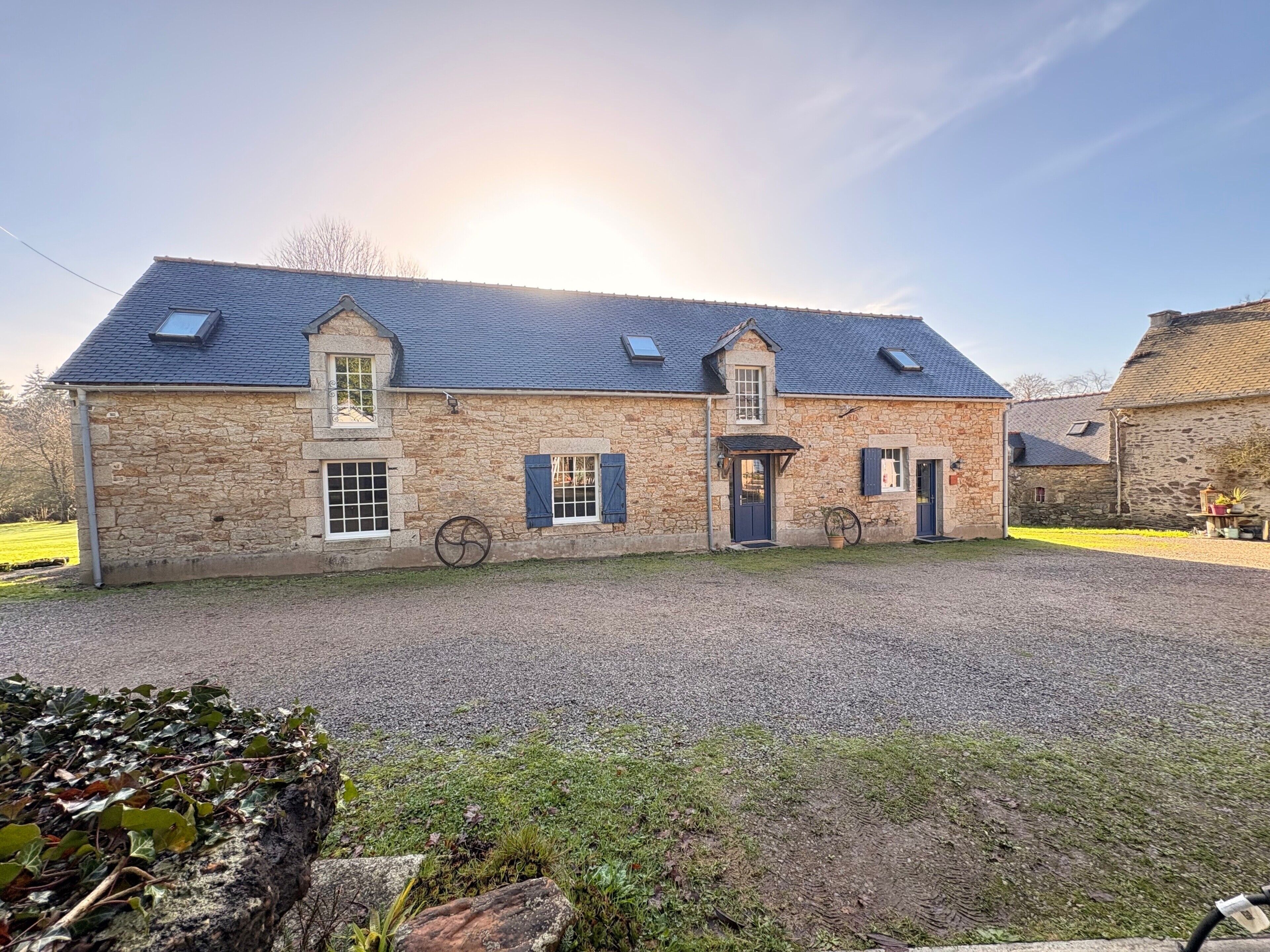 A stone building with a gravel driveway, a bicycle, and a small garden area.