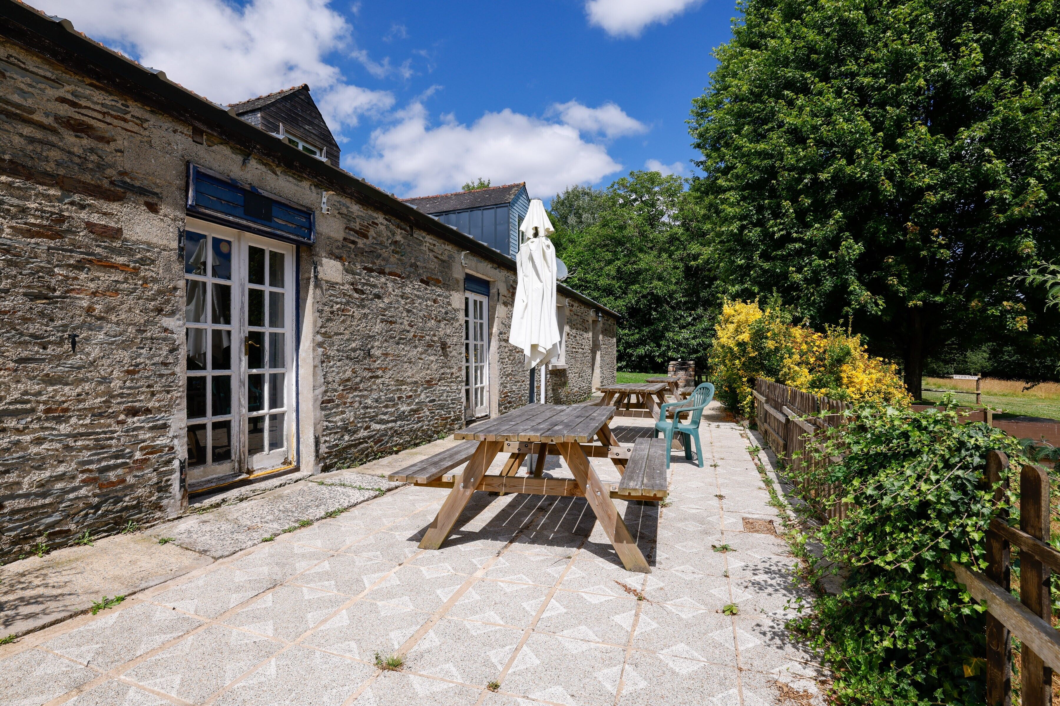 A stone building with a wooden table and chairs, a covered bench, and a wooden fence.