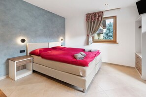 Un dormitorio con cama, mesita de noche y ventana con cortinas.