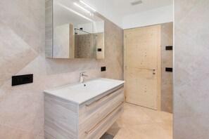Un baño moderno con un espejo grande, un lavamanos blanco y una puerta de madera.
