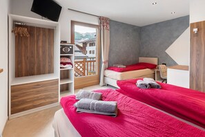 A hotel room with two beds, a wooden wardrobe, a TV, and a view of a mountain.