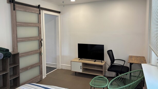 Une chambre à coucher comprenant un lit, une télévision, un bureau, deux chaises, une armoire et un ventilateur de plafond.